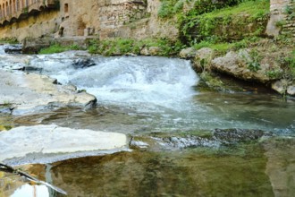 Gentle water flows over smooth stones revealing a tranquil scene. Surrounded by ancient walls and