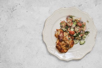 A plate showcases succulent roasted chicken pieces beside a fresh salad made with tomatoes,