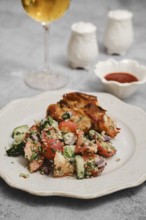 A fresh salad made with tomatoes, cucumbers, and herbs is served alongside grilled chicken