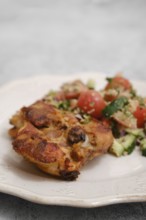 Juicy chicken piece rests on a plate beside a colorful salad made of tomatoes, cucumbers, and herbs