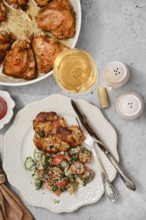 Grilled chicken pieces are plated next to a vibrant salad made of cucumbers and tomatoes. A glass