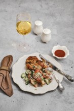 A beautifully arranged meal includes a golden glass of wine, a serving of baked meat, fresh salad