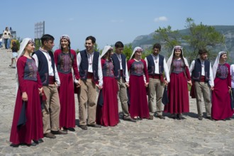 Group in red traditional costumes dancing together on cobblestones against a mountain backdrop,
