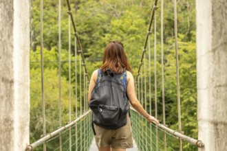 Female tourist with backpack walking on a hanging bridge over the sella river, surrounded by lush