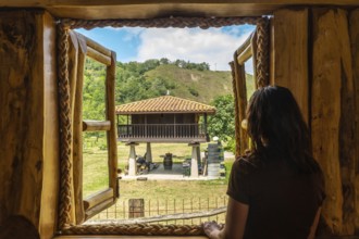 Tourist enjoying the serene view of a traditional asturian horreo from a cozy wooden cabin in the