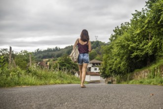 Young woman tourist walking on a road approaching benia de onis village in asturias, spain, during