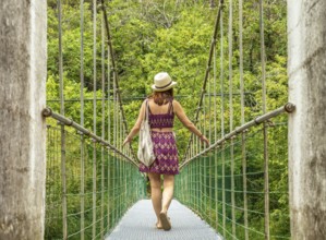 Young woman tourist with a hat and bag walking on a hanging bridge over the dobra river, enjoying a