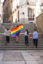 Group of diverse friends celebrating pride, walking up old stairs in a city, carrying a large