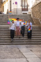 Young friends are celebrating lgbtq plus pride by walking down urban stairs, holding a large