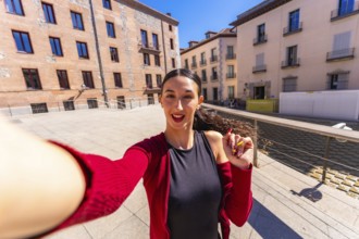 Young woman smiling and holding a smartphone, capturing a selfie portrait in an urban setting