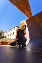 Young woman posing in a modern city environment, featuring rust colored metal structures and