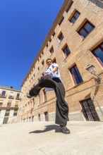 Young man doing a martial arts kick pose with focus and determination, dressed in casual loose