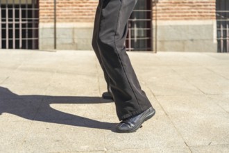 Person's legs moving while dancing outdoors, casting a long shadow on the light colored pavement of