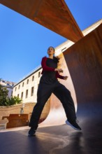 Young woman moving energetically, practicing dance in an urban setting, with modern corten steel