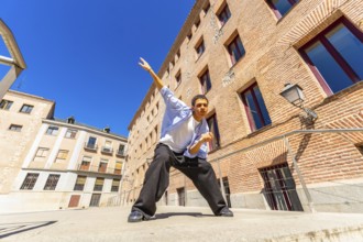 Young man actively posing or dancing in a dynamic stance on a sunny urban street, expressing