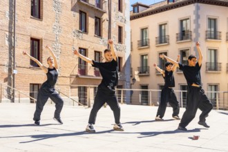 Group of diverse urban dancers performing synchronized street dance movements with raised arms and