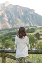 Woman leaning on a wooden fence, admiring the breathtaking view of picu urriellu, a stunning peak