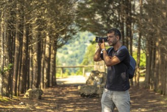Male photographer taking pictures with professional camera in a forest near a viewpoint in benia de