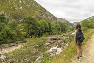 Female tourist with backpack walking along a path next to the sella river, contemplating the