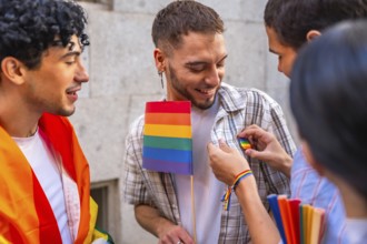 Group of young people smiling and interacting at a pride event, one person receiving a rainbow pin