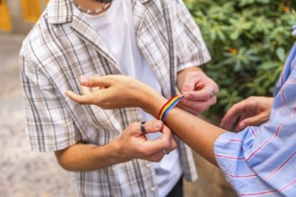 Two hands fastening a colorful rainbow bracelet on a wrist outdoors, symbolizing pride, love and
