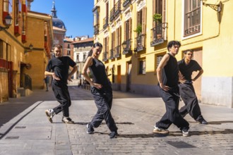 Group of urban dancers in black clothes performing a contemporary dance routine on a cobbled street