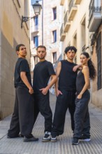 Four young adults in coordinated black streetwear pose confidently on a cobblestone alley, full