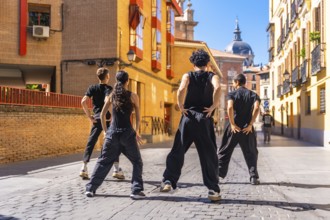 Group of young people standing in an urban cobblestone street, performing an energetic street dance
