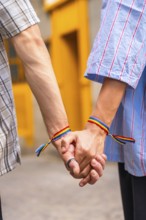 Male couple showing love and support for each other by holding hands with rainbow flag bracelets,