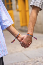 Couple's hands holding together, both wrists featuring rainbow bracelets, symbolizing love, pride,
