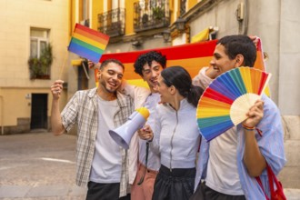 Group of diverse young adults laughing and holding a rainbow flag, a small rainbow flag, a rainbow
