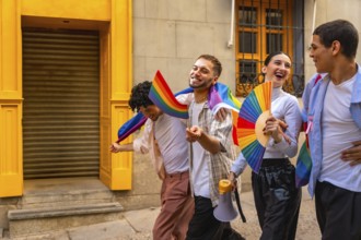 Group of diverse young happy friends walking on a street, celebrating pride day, holding rainbow