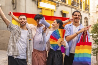 Diverse group of young friends standing together, holding a rainbow flag, fan, and megaphone,