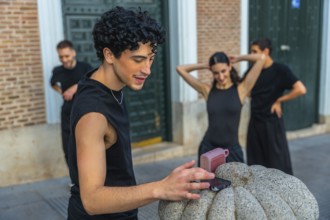 Young man playing music from a smartphone and portable speaker as urban dancers warm up on a city