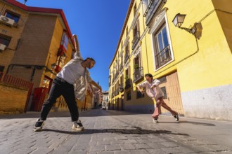 Two young male dancers performing contemporary street dance move on a sunny cobblestone street,
