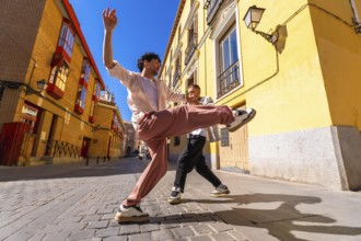 Two energetic young men are performing a dynamic dance routine on a cobblestone street, expressing