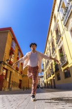 Young man actively dancing with outstretched arms on a sunny cobblestone street, expressing joy and