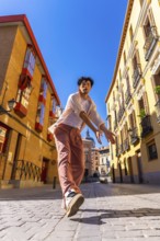Young man striking a dynamic urban dance pose on sunlit cobblestones in madrid, radiating energy,