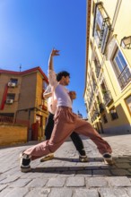 Two young men engaging in an energetic dance performance on a sunny historic cobblestone street,