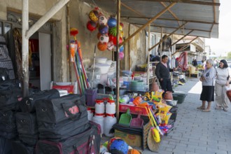 A shopping street with toys and household goods, meat hanging in front of the door, customers