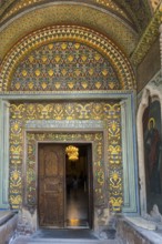 Richly decorated entrance with gold patterns, antique wooden doors and a religious painting, portal