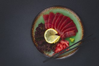 Fresh tuna sashimi served with lemon, wasabi, and pickled ginger on a dark background