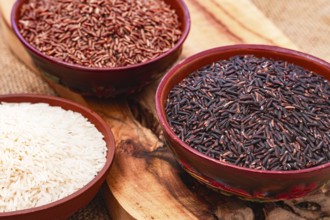 Set of red and black and white rice, in a bowl, on a wooden surface, rustic style, top view