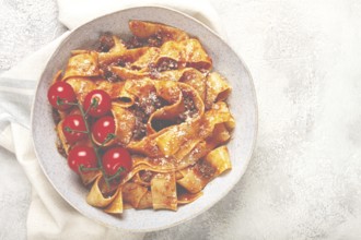 Pappardelle pasta with bolognese sauce, topped with parmesan cheese and cherry branch, homemade, no