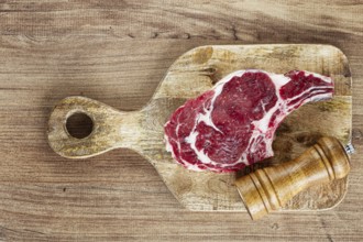 Raw rib eye steak, cowboy steak, on a wooden chopping board, top view, no people