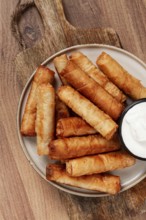 Fried spring rolls with cheese, on a wooden background, with cream sauce, no people