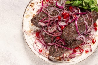 Grilled kebabs topped with onions and pomegranate on a white plate in a bright kitchen setting
