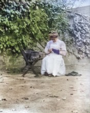Woman in domestic servant housemaid uniform sitting darning in garden setting, c 1900-1920
