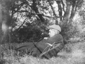Image of pensive young man lying in countryside field with trees c 1910-1920