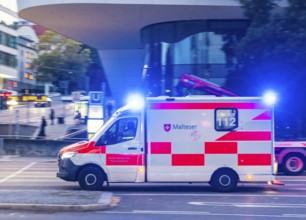 Ambulance of the BOS organisation Malteser with blue lights in an urban environment. Pulling along.